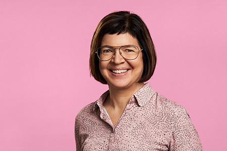 Porträttbild av Hogias skatteexpert Elisabeth Salfjord, som står mot en rosa enfärgad bakgrund. Hon har ett leende ansiktsuttryck.