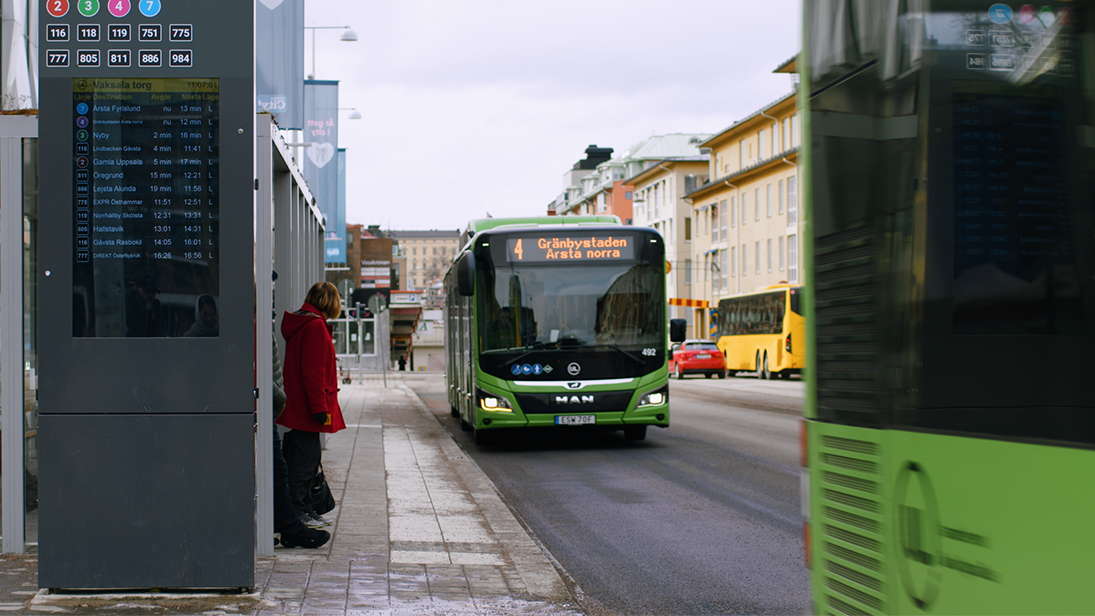 En buss vid hållplats i stadsmiljö med resenär och andra bussar.